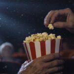 En äldre person bjuder sin stolskompis på biopopcorn.