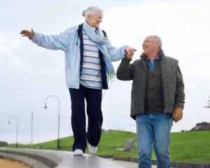 En äldre kvinna balanserar, en äldre man håller henne i handen