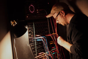 Sander Saarmets står vid en synthesizer och kopplar om sladdar.