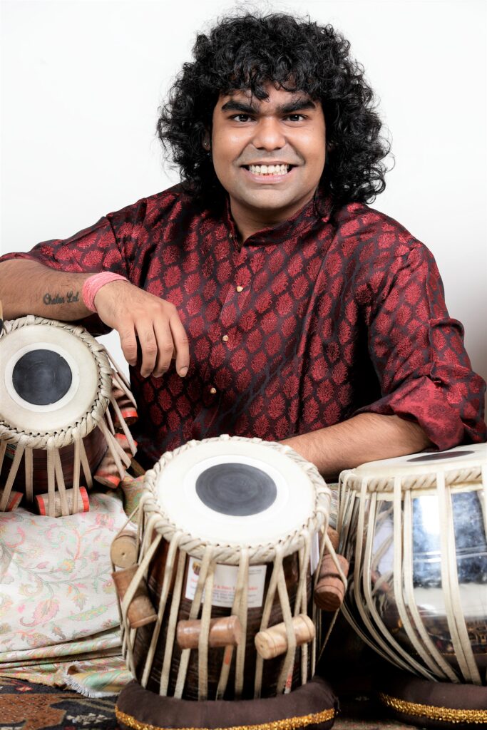 Porträttbild av Pranshu Chatur Lal när han sitter leendes vid sina tablastrummor.