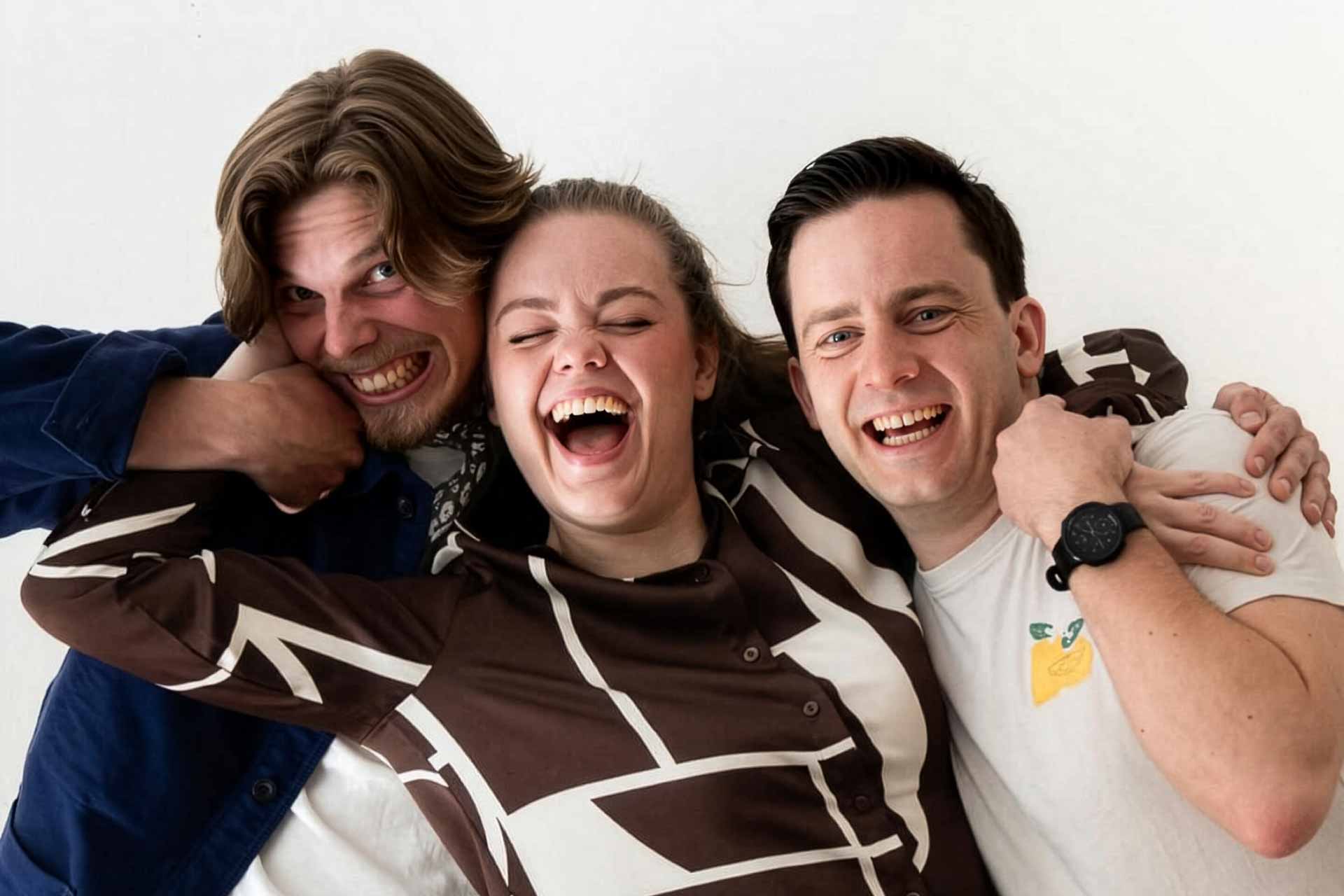 Tre skådespelare som skrattar och kramas
