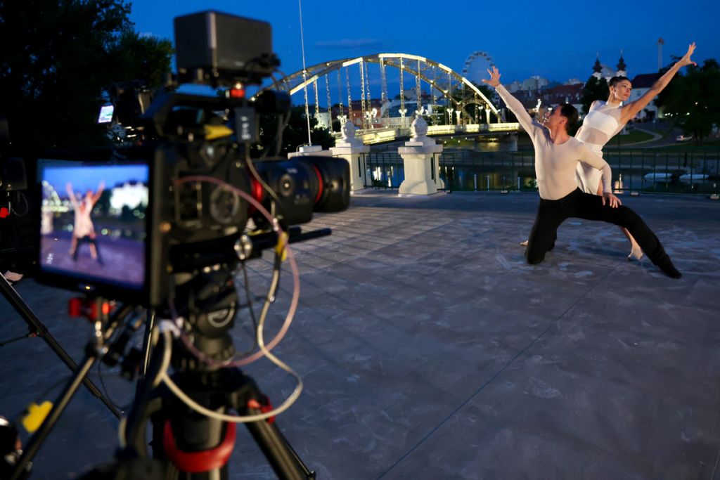 Två dansare dansar framför en upplyst bro och filmas av en kamera.